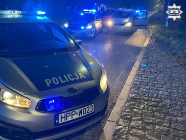 Policyjne radiowozy z włączonymi niebieskimi światłami zatrzymały samochód na drodze nocą.